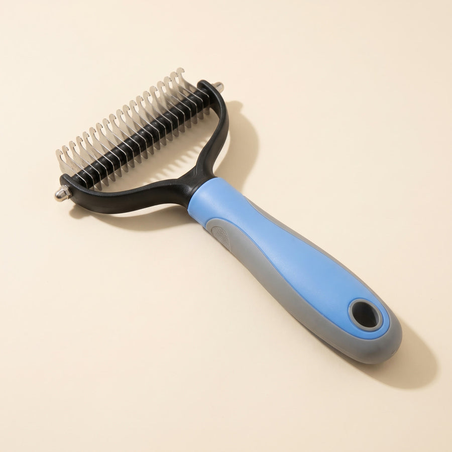 Blue and gray 2-in-1 dematting comb with curved steel blades, on a plain cream background