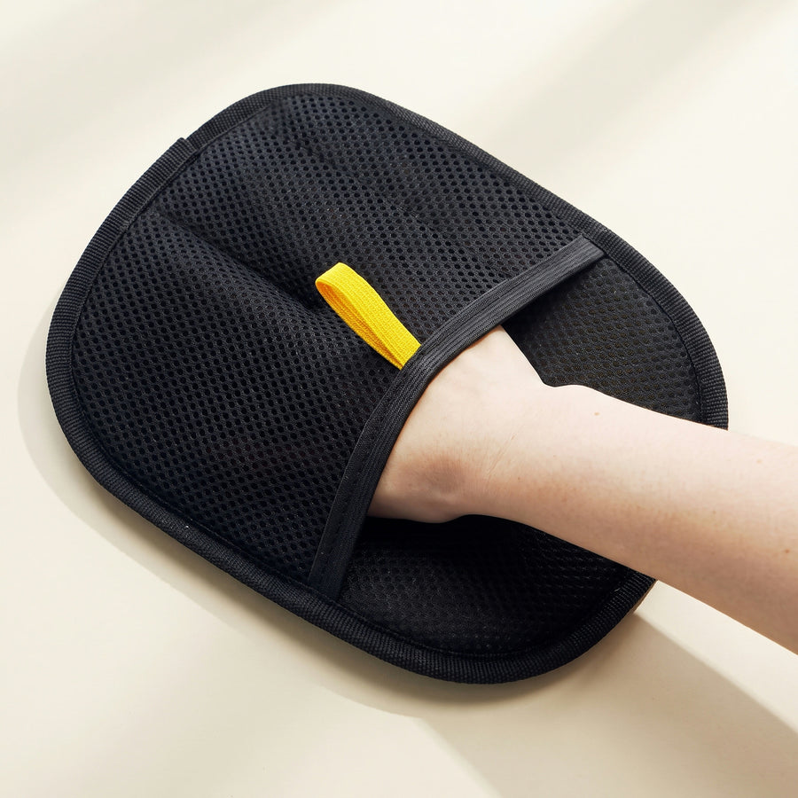 Black pet hair remover glove on a hand, fine perforated mesh and the yellow pull tab