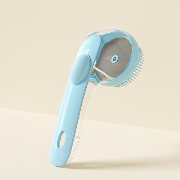 Blue silicone bath brush with a clear shampoo reservoir handle, press button and round bristle head, on a plain cream background